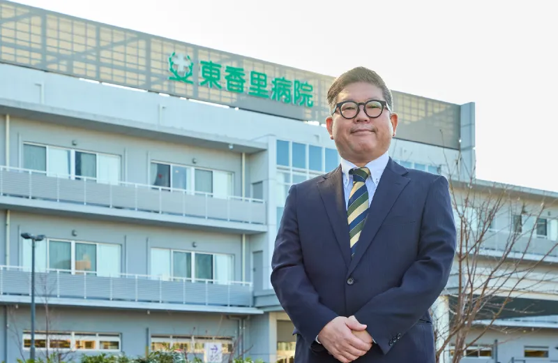 病棟前にて、柔らかな笑顔を見せる田場氏